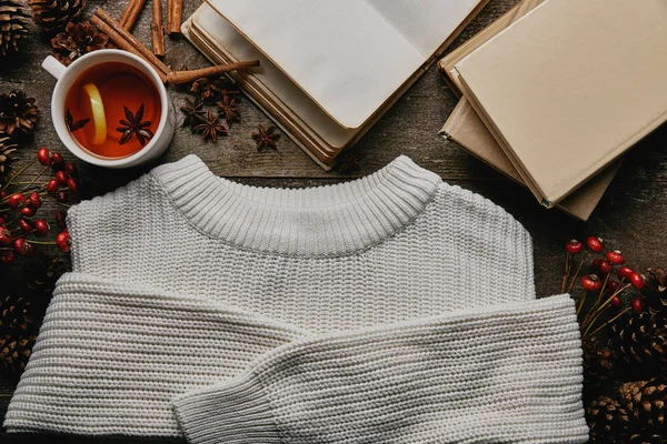 Flat lay com suéter branco, cones de pinho, paus de canela, xícara de chá e livros na superfície de madeira — Fotografia de Stock