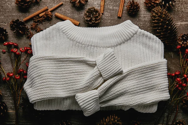Flat lay with white sweater, pine cones, cinnamon sticks and red holly berries on wooden surface — Stock Photo