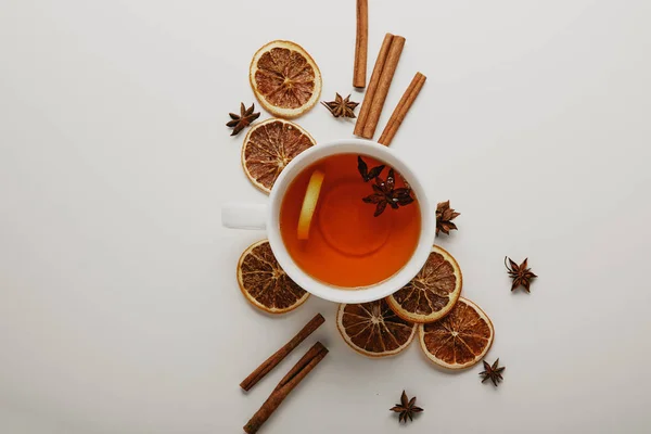 Posa piatta con bastoncini di cannella disposti, stelle di anice, pezzi di arancia secca e una tazza di tè caldo su sfondo bianco — Foto stock