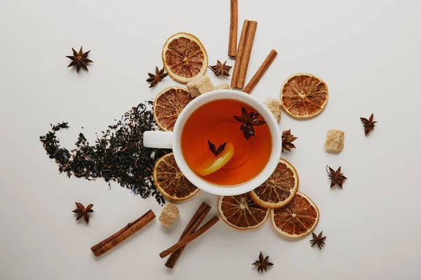 Acostado plano con palos de canela arreglados, estrellas de anís, azúcar morena y taza de té caliente sobre fondo blanco - foto de stock