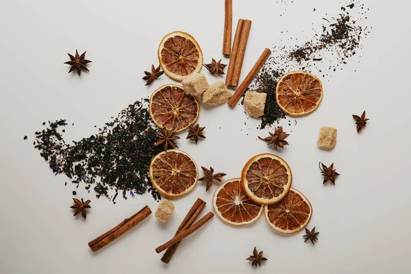 Tendido plano con arreglo de piezas de naranja seca, palitos de canela, estrellas de anís y azúcar morena sobre fondo blanco - foto de stock