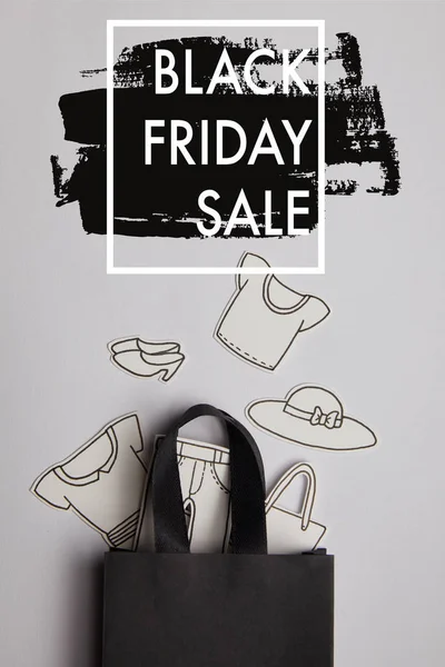 Top view of black shopping bag and paper clothes on grey background, black friday sale concept — Stock Photo