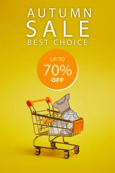 Close up view of little shopping trolley with paper clothes on yellow backdrop, ssss inscription — Stock Photo