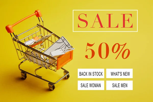 Close up view of little shopping trolley with paper clothes on yellow backdrop, sale banner concept — Stock Photo