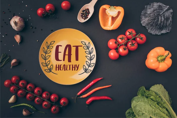 Vue du dessus de poivrons et tomates cerises avec assiette jaune avec manger lettrage sain sur table grise — Photo de stock