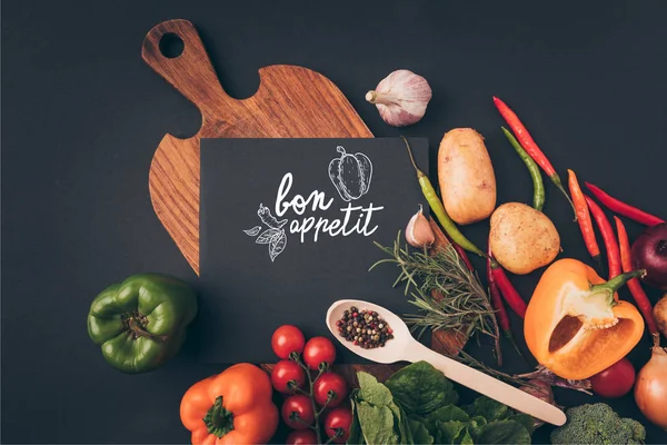 Vue du dessus du tableau noir sur table en bois avec légumes sur table grise, lettrage appétit bon — Photo de stock