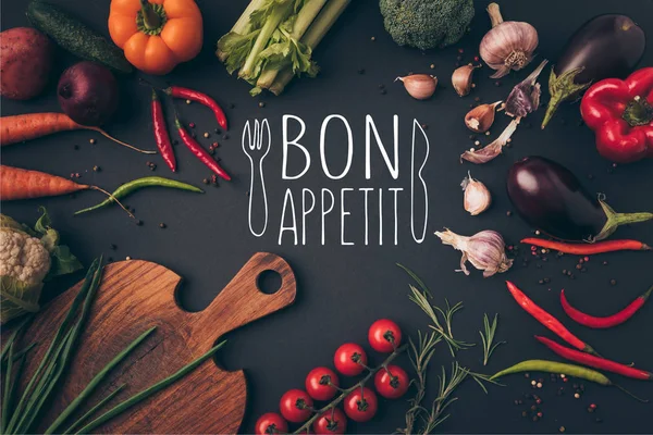 Top view of different vegetables and cutting board on table with bon appetit lettering — Stock Photo