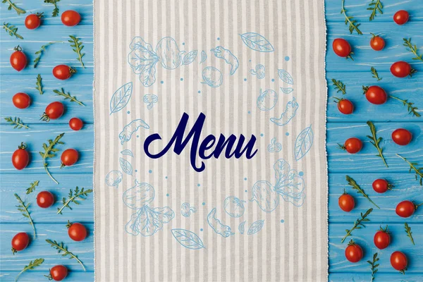 Top view of napkin and cherry tomatoes with arugula on blue table, menu lettering — Stock Photo