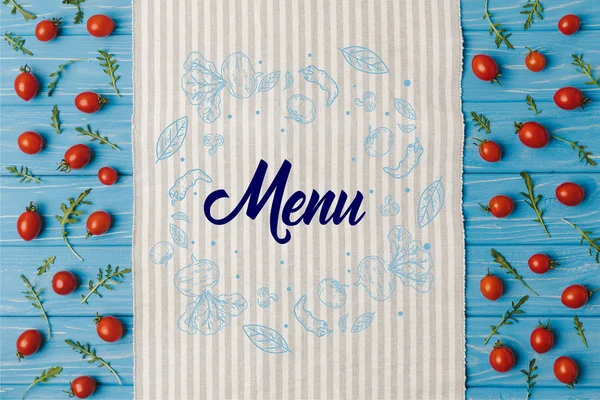 Верхний вид на салфетку и помидоры черри с рукколой на голубом столе, надпись на меню — стоковое фото