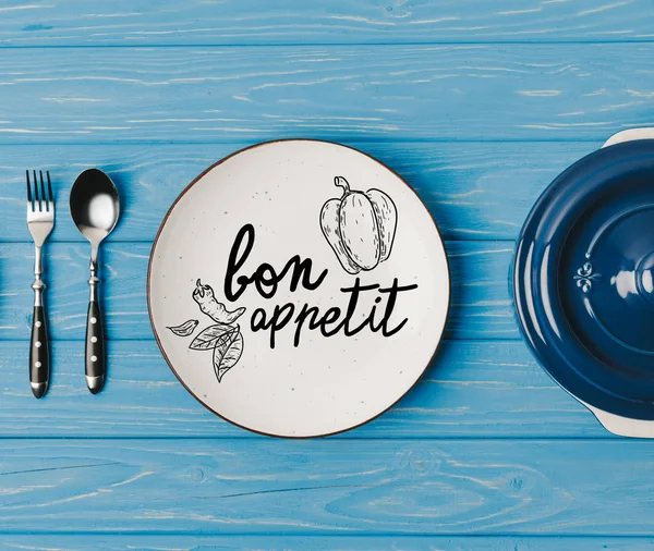 Draufsicht auf Gabel, Löffel und Teller auf blauem Tisch, leckerer Appetit-Schriftzug — Stockfoto