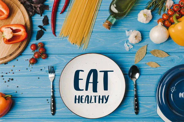 Top view of ingredients for cooking pasta on blue table, eat healthy lettering — Stock Photo