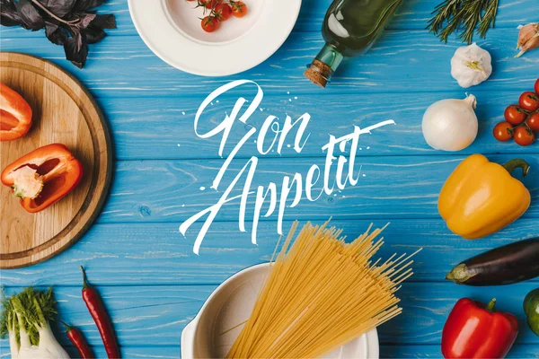 Draufsicht auf ungekochte Pasta und Gemüse auf blauem Tisch, Guten Appetit Schriftzug — Stockfoto