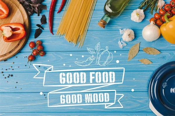 Vista superior de los ingredientes para cocinar pasta en la mesa azul, buena comida letras de buen humor - foto de stock