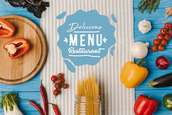Vista superior de massas não cozidas e legumes maduros em guardanapo na mesa azul, delicioso menu restaurante lettering — Fotografia de Stock