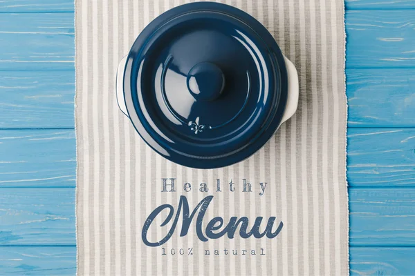 Top view of pan on napkin on blue wooden table, healthy menu lettering — Stock Photo