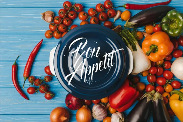 Draufsicht auf Pfanne zwischen Gemüse auf blauem Tisch, Guten Appetit Schriftzug — Stockfoto