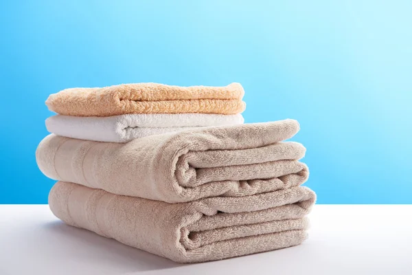 Close-up view of stacked clean towels on white table on blue — Stock Photo