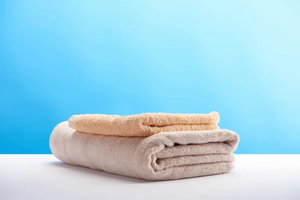 Stacked clean towels on white table on blue background — Stock Photo