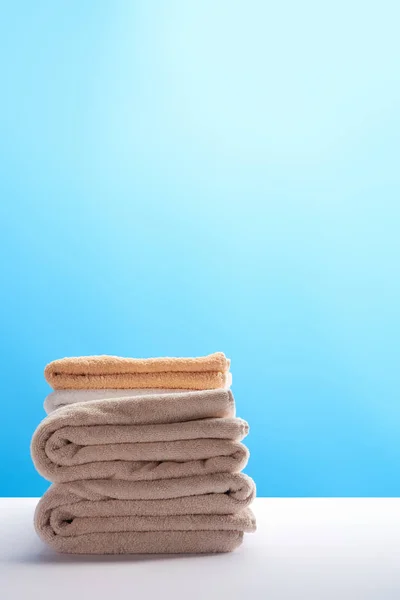 Pila de toallas limpias y frescas sobre una mesa blanca sobre fondo azul - foto de stock