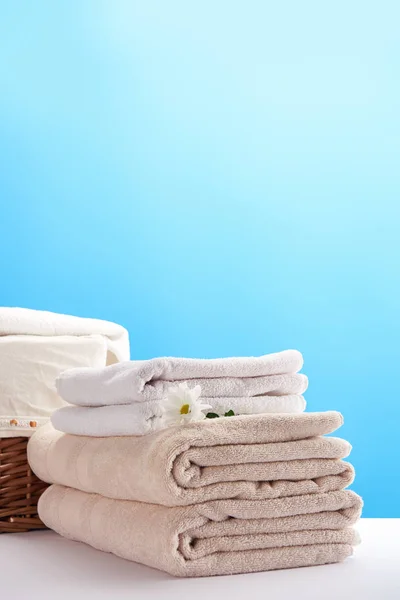 Vista ravvicinata di asciugamani, bel fiore di camomilla e cesto della lavanderia su blu — Foto stock