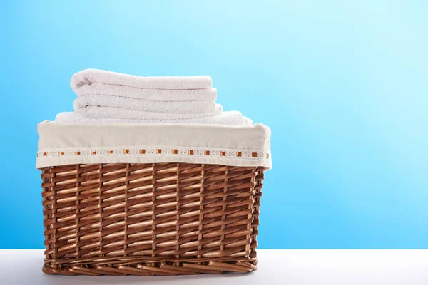 Vista de cerca de la cesta de la ropa con toallas suaves limpias sobre fondo azul - foto de stock