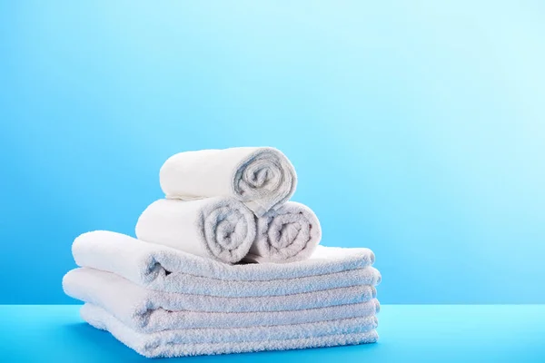 Rolled and stacked clean white towels on blue — Stock Photo