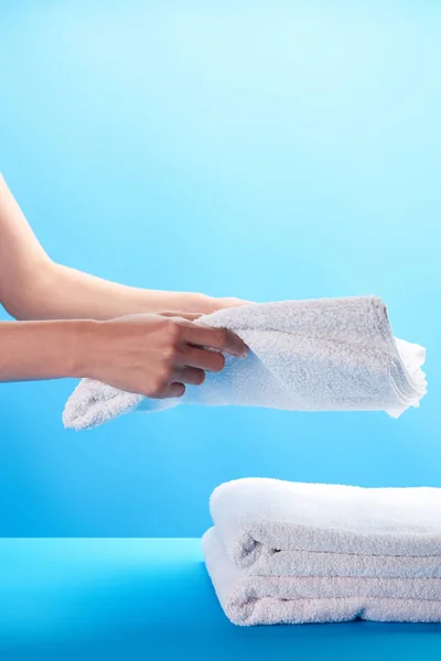 Vista parziale di persona accatastamento asciugamani bianchi puliti su blu — Foto stock