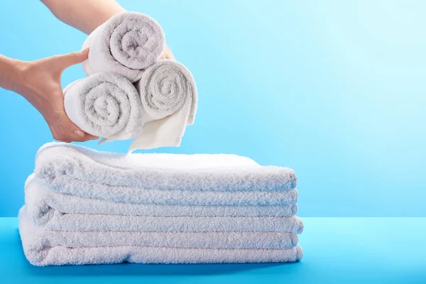 Cropped shot of person holding rolled white towels above pile of towels on blue — Stock Photo