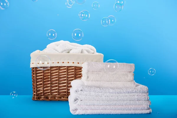 Serviettes blanches propres, panier à linge et bulles de savon sur bleu — Photo de stock