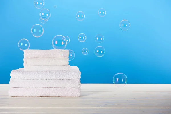 Toallas blancas suaves limpias y burbujas de jabón sobre fondo azul - foto de stock