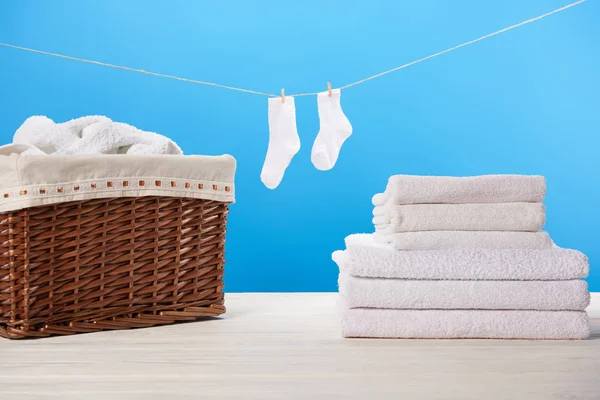 Cesta de roupa, pilha de toalhas macias limpas e meias brancas penduradas na corda em azul — Fotografia de Stock