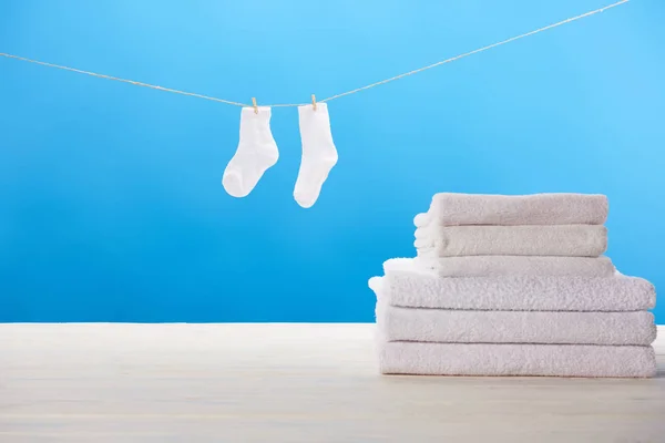 Pile of soft towels and clean white socks hanging on clothesline on blue background — Stock Photo