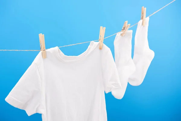 Calcetines blancos limpios y camiseta colgando en tendedero aislado en azul - foto de stock