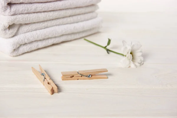 Vista de cerca de pinzas de ropa, hermosa flor de manzanilla y toallas suaves limpias en mesa de madera blanca - foto de stock