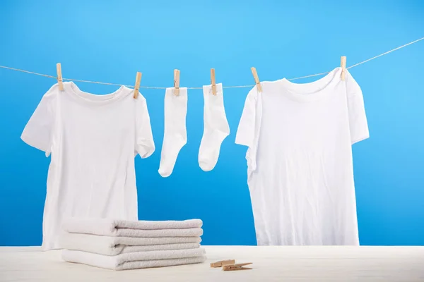 Pile on clean towels, clothespins and white clothes hanging on rope on blue — Stock Photo