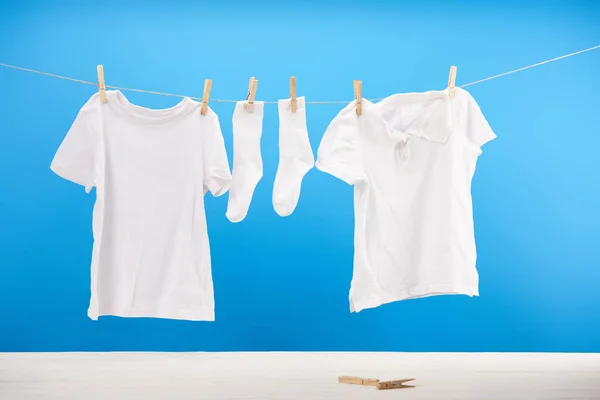 Чисті білі шкарпетки та футболки, що висять на лінії одягу на синьому — стокове фото