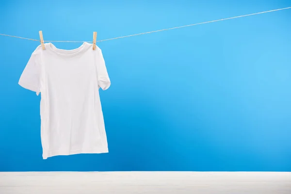 Clean white t-shirt hanging on rope on blue — Stock Photo