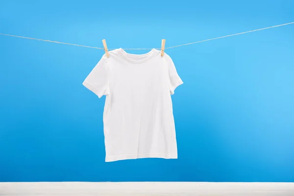 Clean white t-shirt hanging on clothesline on blue — Stock Photo