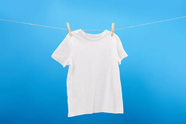 T-shirt blanc avec pinces à linge suspendues sur corde à linge isolée sur bleu — Photo de stock