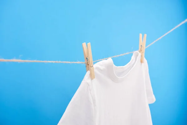 Camiseta blanca limpia con pinzas de ropa colgando de una cuerda aislada en azul - foto de stock