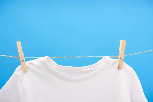 Vista de cerca de la camiseta blanca limpia con pinzas de ropa colgando de una cuerda aislada en azul - foto de stock