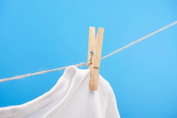 Vista de cerca de la camiseta blanca limpia con pinza de ropa colgando de una cuerda aislada en azul - foto de stock