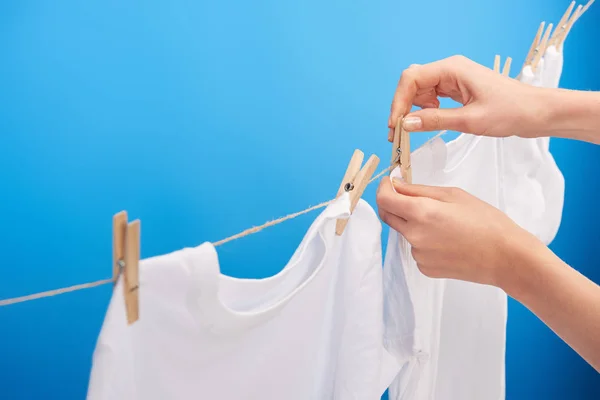 Tiro recortado de la persona colgando ropa limpia con pinzas de ropa en el tendedero aislado en azul - foto de stock