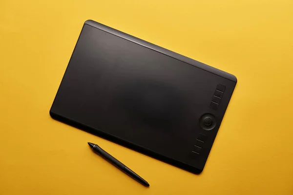 Vista superior de la tableta gráfica y la pluma en la superficie amarilla - foto de stock