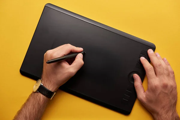 Recortado tiro de hombre dibujo con gráficos tableta en la superficie amarilla - foto de stock