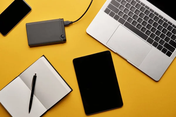 Vue de dessus de divers gadgets avec ordinateur portable ouvert couché sur la surface jaune — Photo de stock