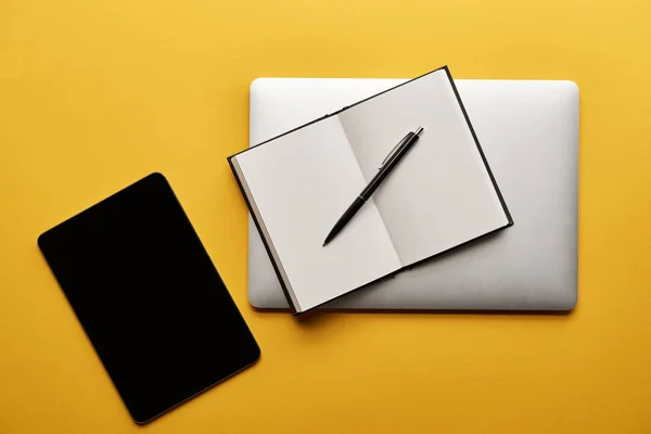 Draufsicht auf drahtlose Geräte mit leerem Notizbuch auf gelber Oberfläche — Stockfoto
