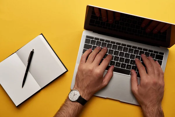 Cropped shot of man working with laptop and notebook on yellow surface — Stock Photo