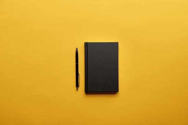 Top view of closed notebook and pen on yellow surface — Stock Photo