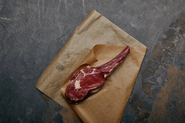 Draufsicht auf Roh-Rib-Eye-Steak auf Backpapier auf grauem Hintergrund — Stockfoto